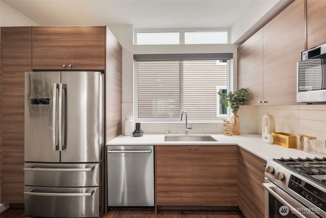 kitchen featuring a sink, tasteful backsplash, stainless steel appliances, brown cabinetry, and light countertops