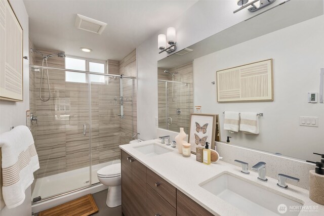 bathroom with double vanity, toilet, a stall shower, and a sink