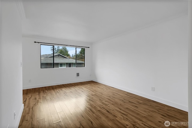 empty room featuring wood finished floors, baseboards, and ornamental molding