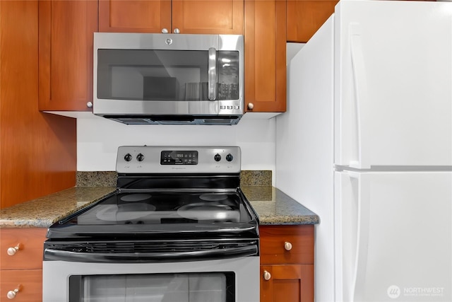 kitchen with brown cabinets, appliances with stainless steel finishes, and dark stone countertops