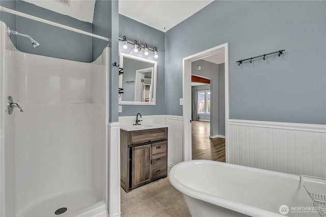 full bathroom with vanity, a shower stall, a soaking tub, and a wainscoted wall