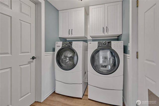 laundry area featuring washer and clothes dryer, cabinet space, wainscoting, and light wood-style floors