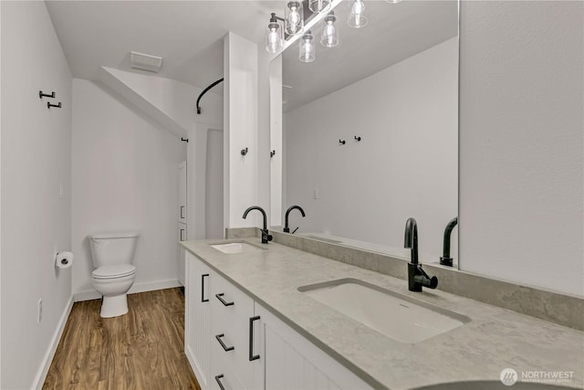 full bath with double vanity, wood finished floors, toilet, and a sink