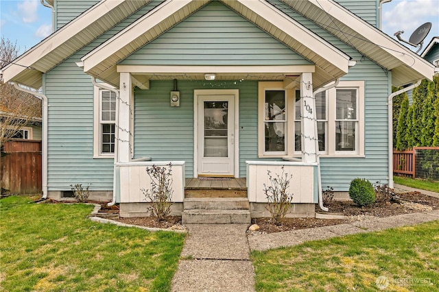 entrance to property with a lawn, covered porch, and fence