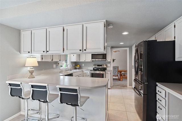 kitchen with light tile patterned floors, appliances with stainless steel finishes, white cabinetry, and a peninsula