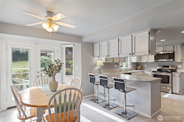 kitchen with a breakfast bar area, light tile patterned floors, a peninsula, stainless steel appliances, and light countertops