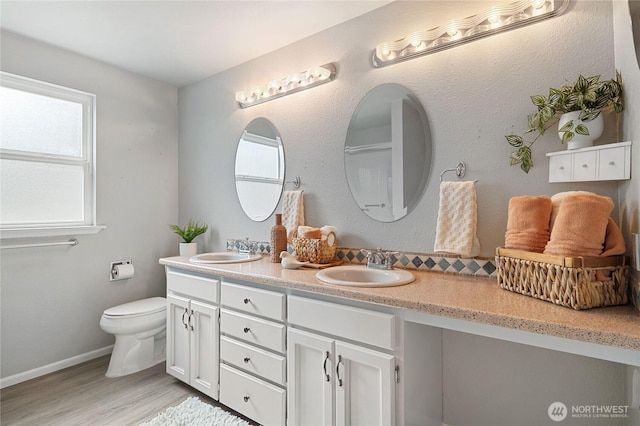 full bathroom with double vanity, toilet, wood finished floors, and a sink