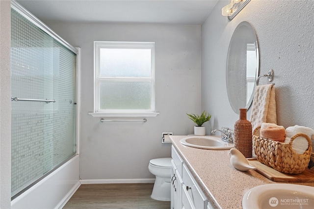 full bathroom with baseboards, toilet, double vanity, wood finished floors, and a sink