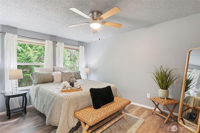 bedroom featuring ceiling fan, a textured ceiling, baseboards, and wood finished floors