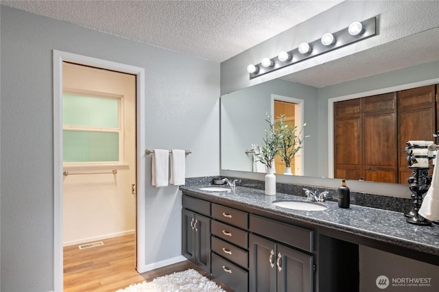 bathroom with wood finished floors, visible vents, double vanity, a sink, and a textured ceiling