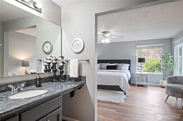 ensuite bathroom with baseboards, vanity, wood finished floors, a textured ceiling, and ensuite bath