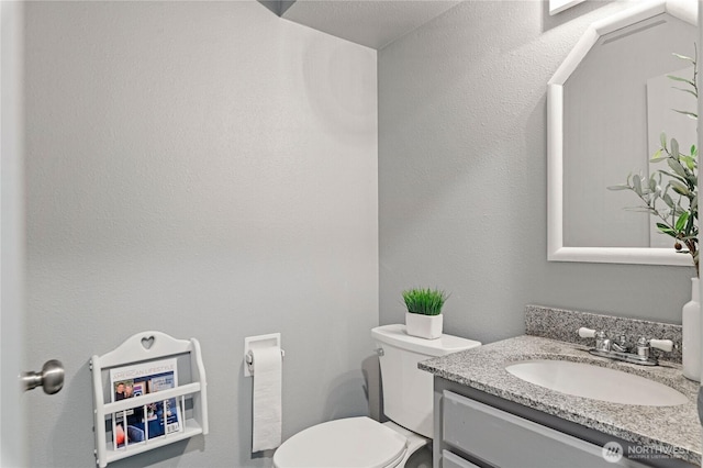 bathroom with toilet, vanity, and a textured wall