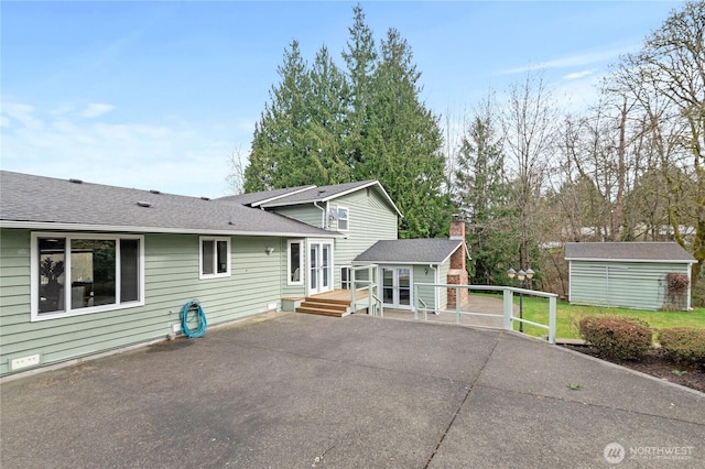 back of property featuring aphalt driveway, a patio, an outdoor structure, a wooden deck, and a chimney