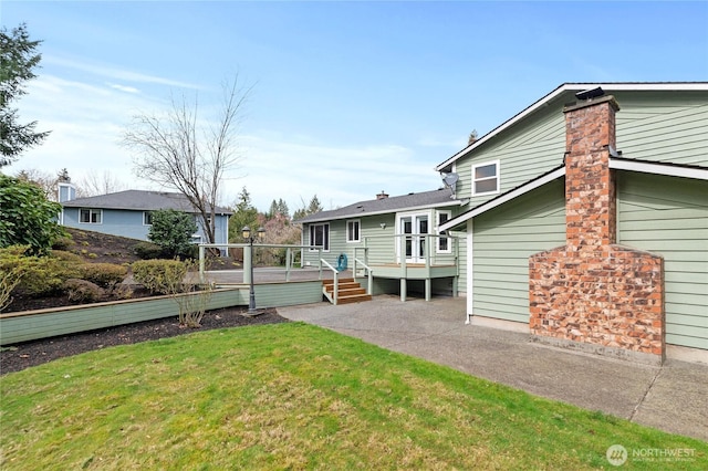 rear view of property with a wooden deck, a patio, a lawn, and a chimney