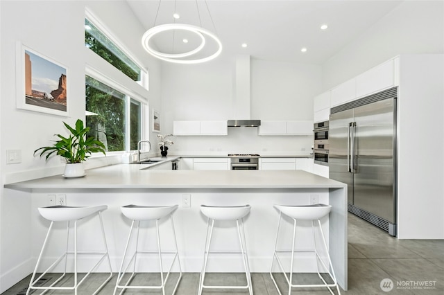 kitchen with light countertops, a peninsula, white cabinets, stainless steel appliances, and a sink