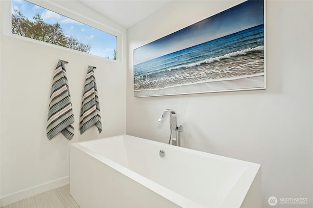 bathroom with baseboards, a freestanding bath, and tile patterned flooring