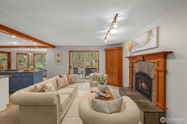 living room with beam ceiling, rail lighting, a wealth of natural light, and a tile fireplace