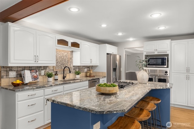 kitchen featuring a sink, stainless steel appliances, light stone countertops, and a breakfast bar