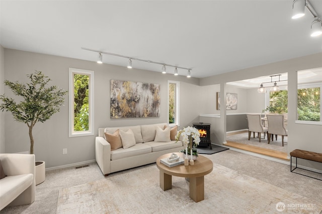 living room featuring carpet, visible vents, baseboards, a wood stove, and track lighting