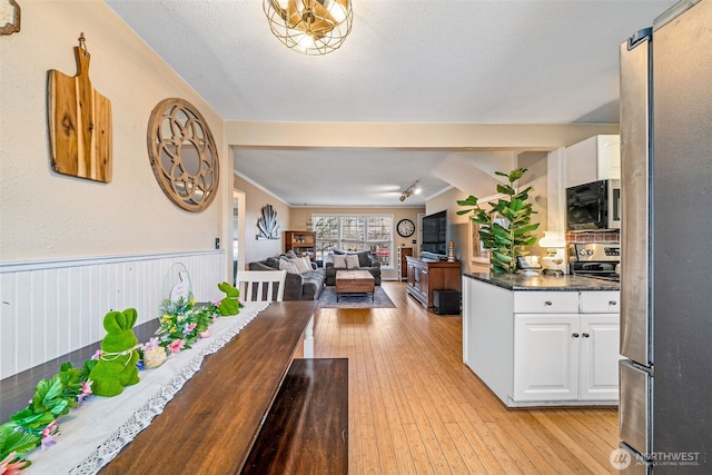 kitchen featuring stainless steel appliances, light wood-style floors, wainscoting, white cabinetry, and dark countertops