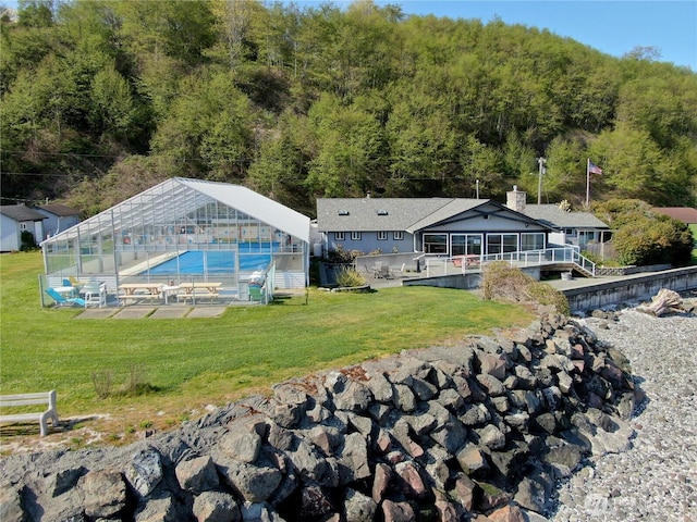 back of property featuring a greenhouse, a chimney, an outdoor structure, and a yard