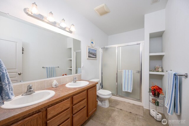 bathroom featuring double vanity, a stall shower, toilet, and a sink