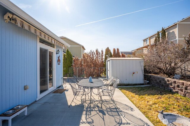 view of patio with an outbuilding, outdoor dining space, a storage unit, and fence