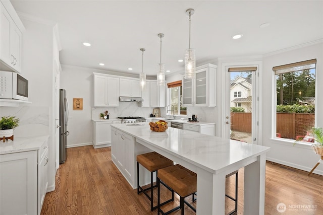 kitchen with decorative backsplash, white cabinets, under cabinet range hood, and stainless steel appliances