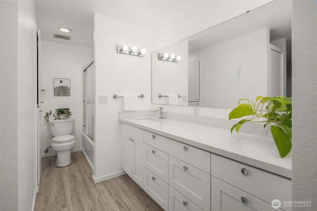 bathroom featuring visible vents, toilet, wood finished floors, shower / bath combination with glass door, and vanity