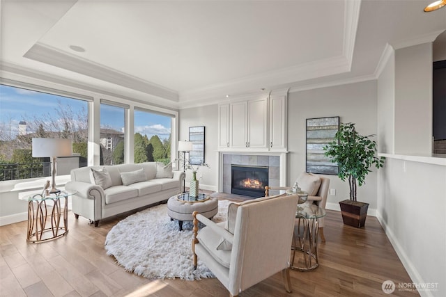 living area with crown molding, a fireplace, a raised ceiling, and light wood-style floors