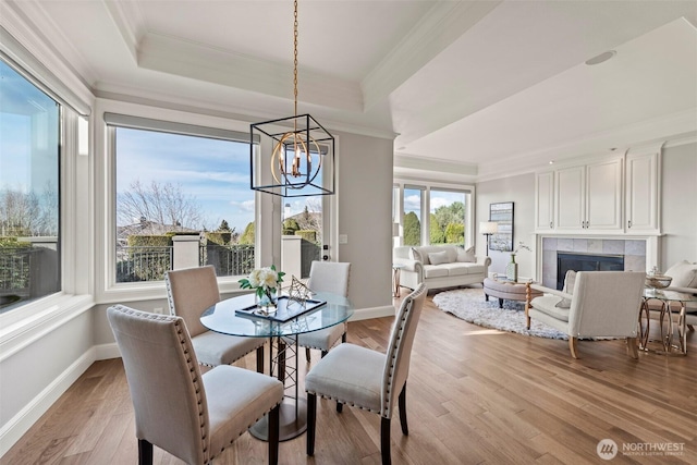 dining space with a tile fireplace, a raised ceiling, light wood-style floors, and ornamental molding