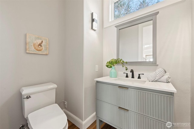 half bathroom with vanity, toilet, and baseboards