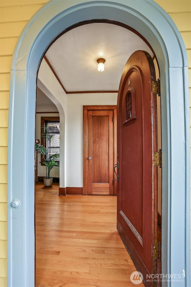 corridor featuring arched walkways, light wood-type flooring, baseboards, and ornamental molding