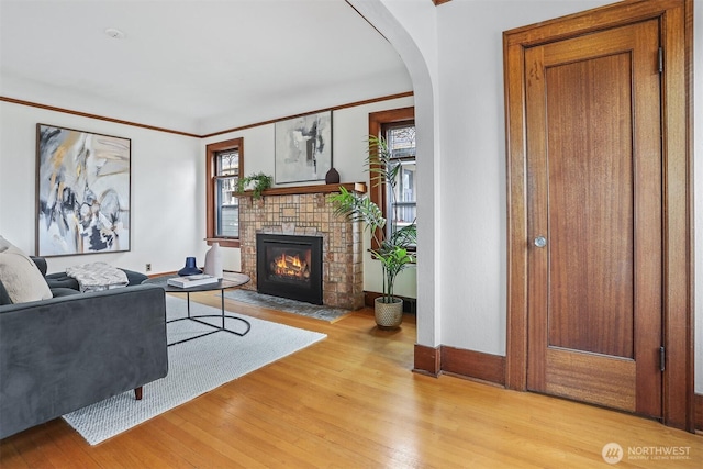 living room with light wood-type flooring, plenty of natural light, a brick fireplace, and ornamental molding