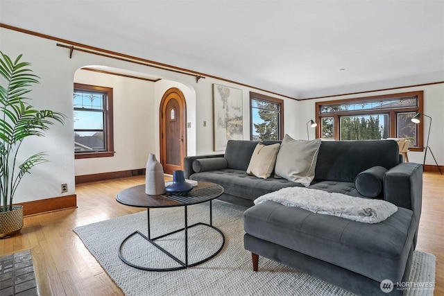 living area featuring arched walkways, crown molding, baseboards, and wood finished floors