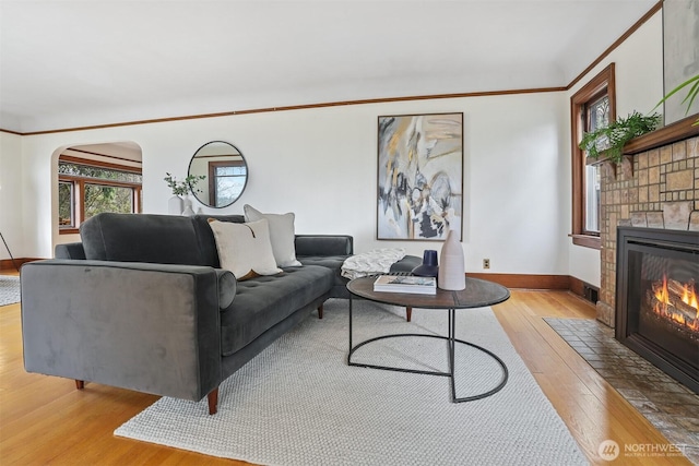 living area with baseboards, a fireplace with flush hearth, ornamental molding, hardwood / wood-style flooring, and arched walkways