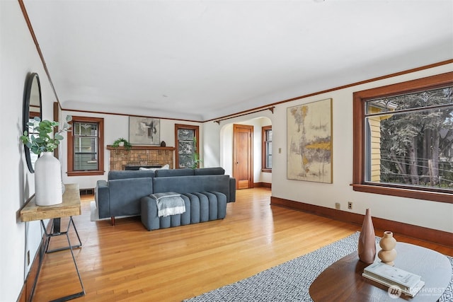 living room featuring arched walkways, light wood-style floors, a fireplace, crown molding, and baseboards