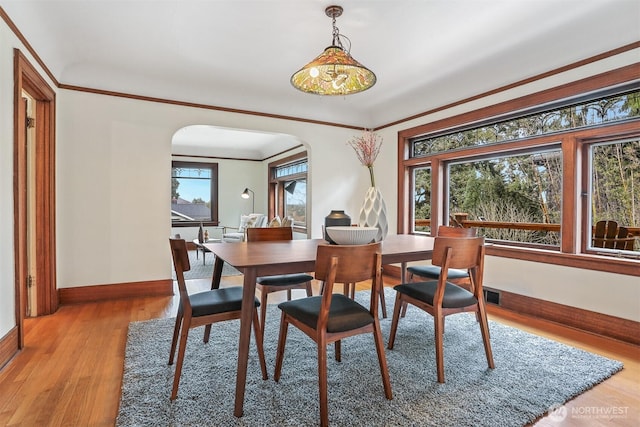 dining room featuring crown molding, arched walkways, a wealth of natural light, and light wood-type flooring