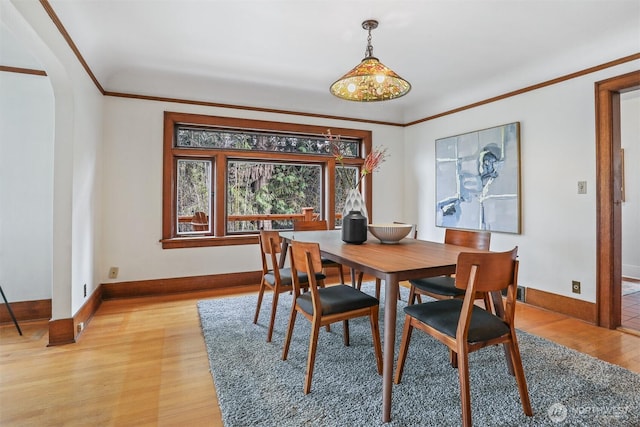 dining room featuring crown molding, light wood-style flooring, baseboards, and arched walkways