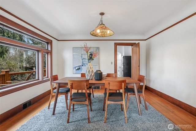 dining area with crown molding, wood finished floors, visible vents, and baseboards