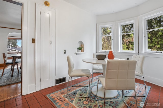 dining space with dark tile patterned floors, arched walkways, visible vents, and baseboards