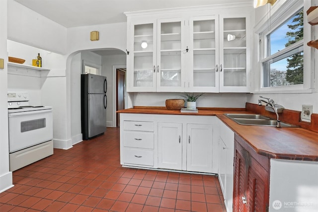 kitchen with electric stove, a sink, freestanding refrigerator, arched walkways, and white cabinets