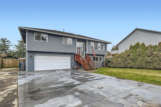 split foyer home featuring an attached garage, concrete driveway, a front lawn, and fence