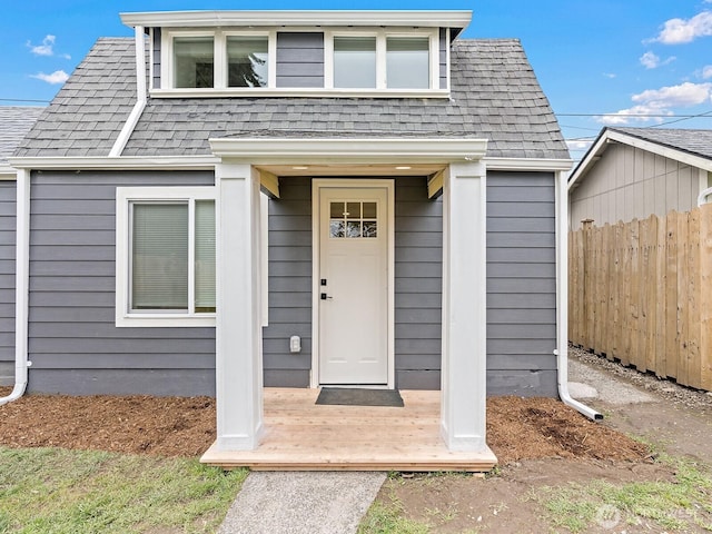 doorway to property featuring fence and roof with shingles