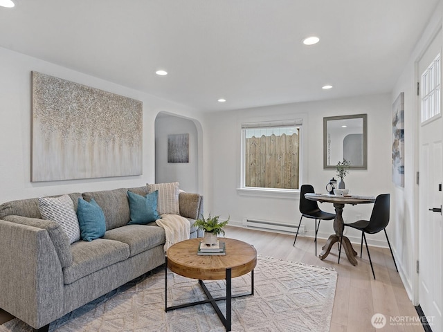 living area with light wood-type flooring, recessed lighting, arched walkways, a baseboard radiator, and baseboards