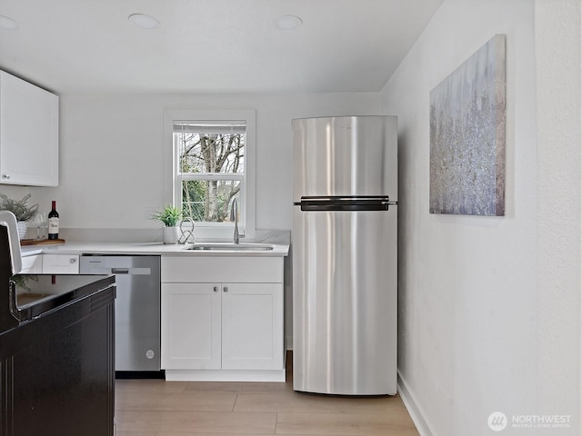 kitchen featuring white cabinets, appliances with stainless steel finishes, light countertops, and a sink