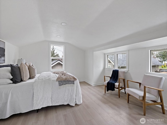 bedroom with lofted ceiling, multiple windows, baseboards, and light wood finished floors