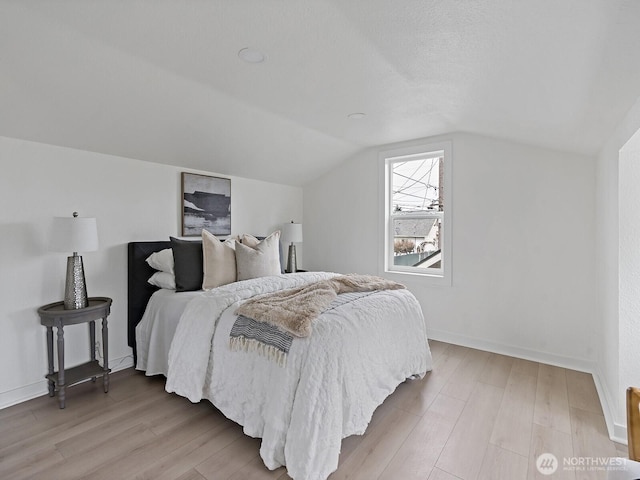 bedroom featuring lofted ceiling, baseboards, and light wood finished floors