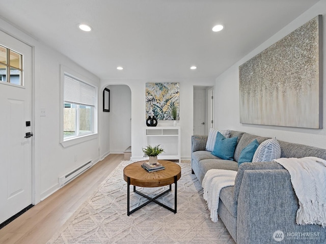 living room featuring baseboards, light wood-style flooring, recessed lighting, arched walkways, and a baseboard heating unit