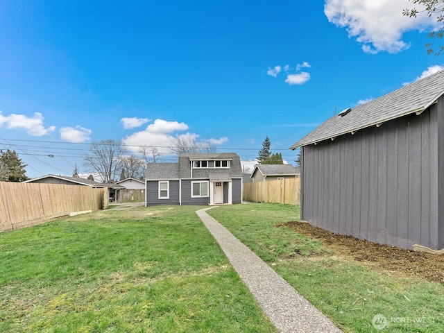 rear view of property featuring an outbuilding, a lawn, a fenced backyard, and roof with shingles